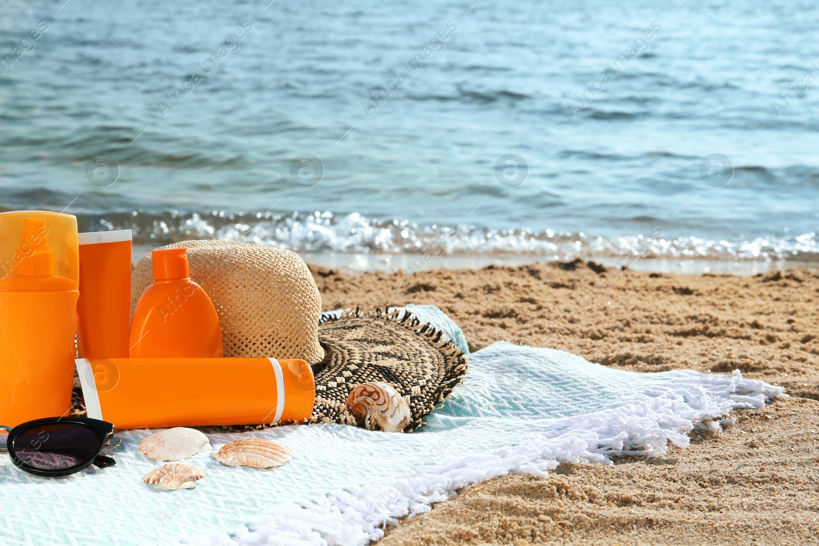 Photo of Sun protection products and beach accessories on blanket near sea, space for text