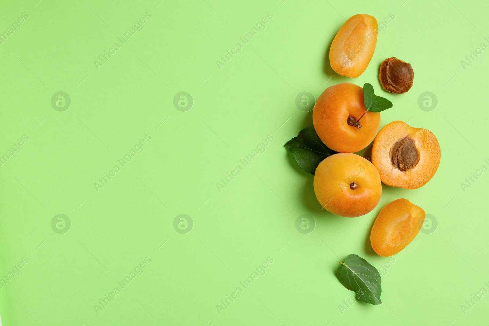 Photo of Delicious ripe sweet apricots on green background, flat lay. Space for text