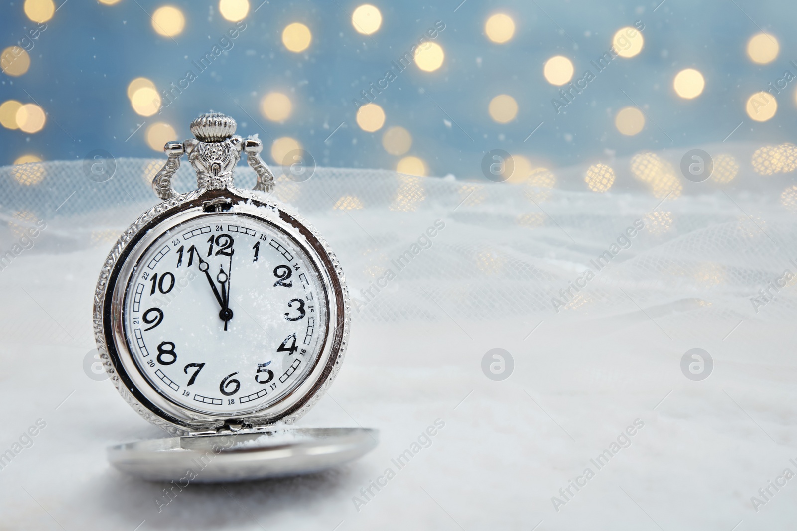 Photo of Pocket watch with snow on table against blurred lights. Christmas countdown