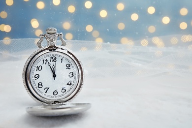 Photo of Pocket watch with snow on table against blurred lights. Christmas countdown