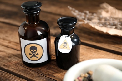 Photo of Glass bottles of poison with warning signs on wooden table