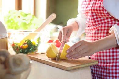 Photo of Woman cutting fresh lemon at countertop in kitchen, closeup
