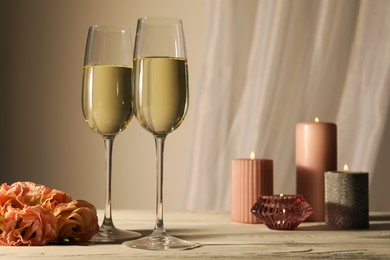 Glasses of sparkling wine, flowers and burning candles on white table