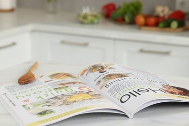 Photo of Open culinary magazine on white table in kitchen, closeup. Space for text
