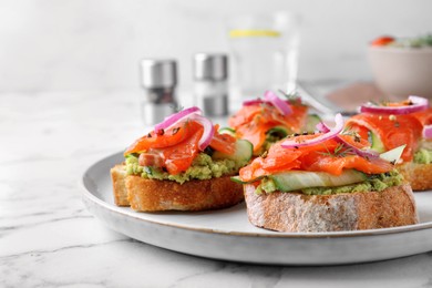 Delicious sandwiches with salmon, avocado, cucumber and onion on white marble table, closeup