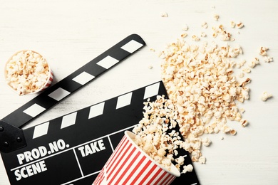 Tasty popcorn and clapperboard on wooden background, top view. Cinema snack