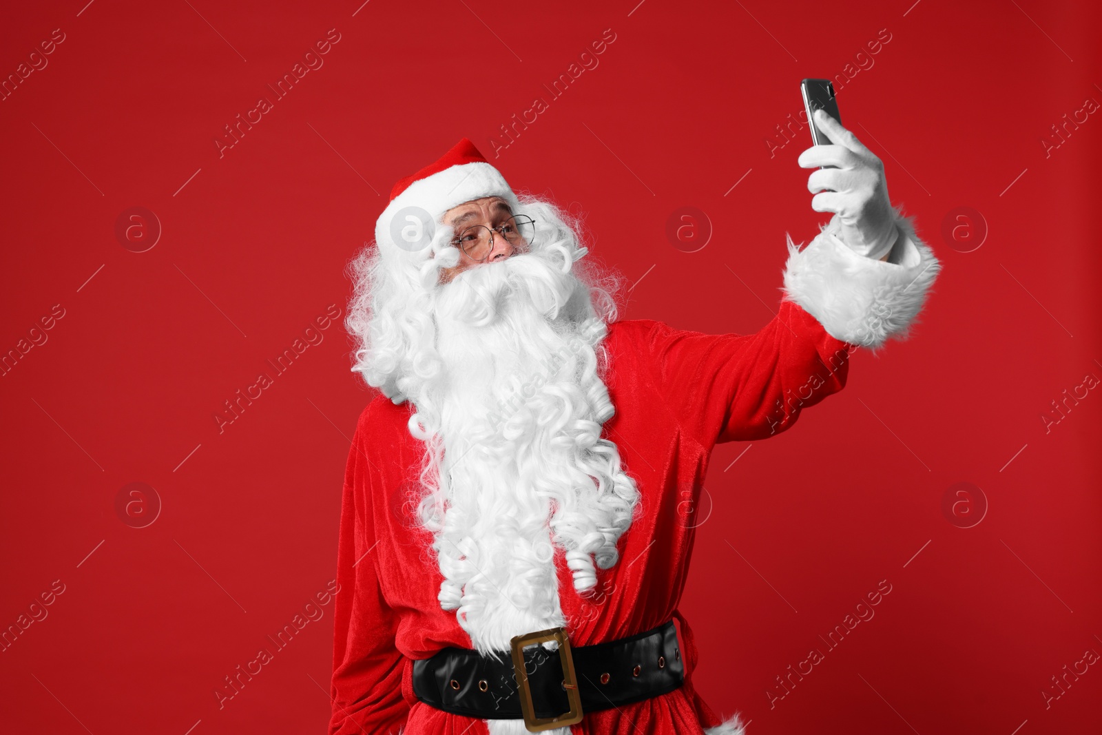 Photo of Merry Christmas. Santa Claus taking selfie on red background