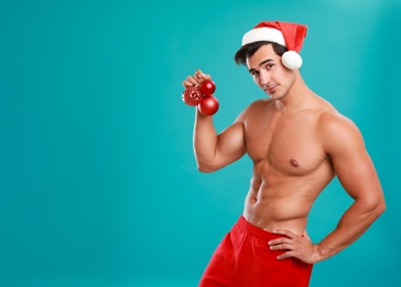 Photo of Sexy shirtless Santa Claus with Christmas balls on blue background, space for text