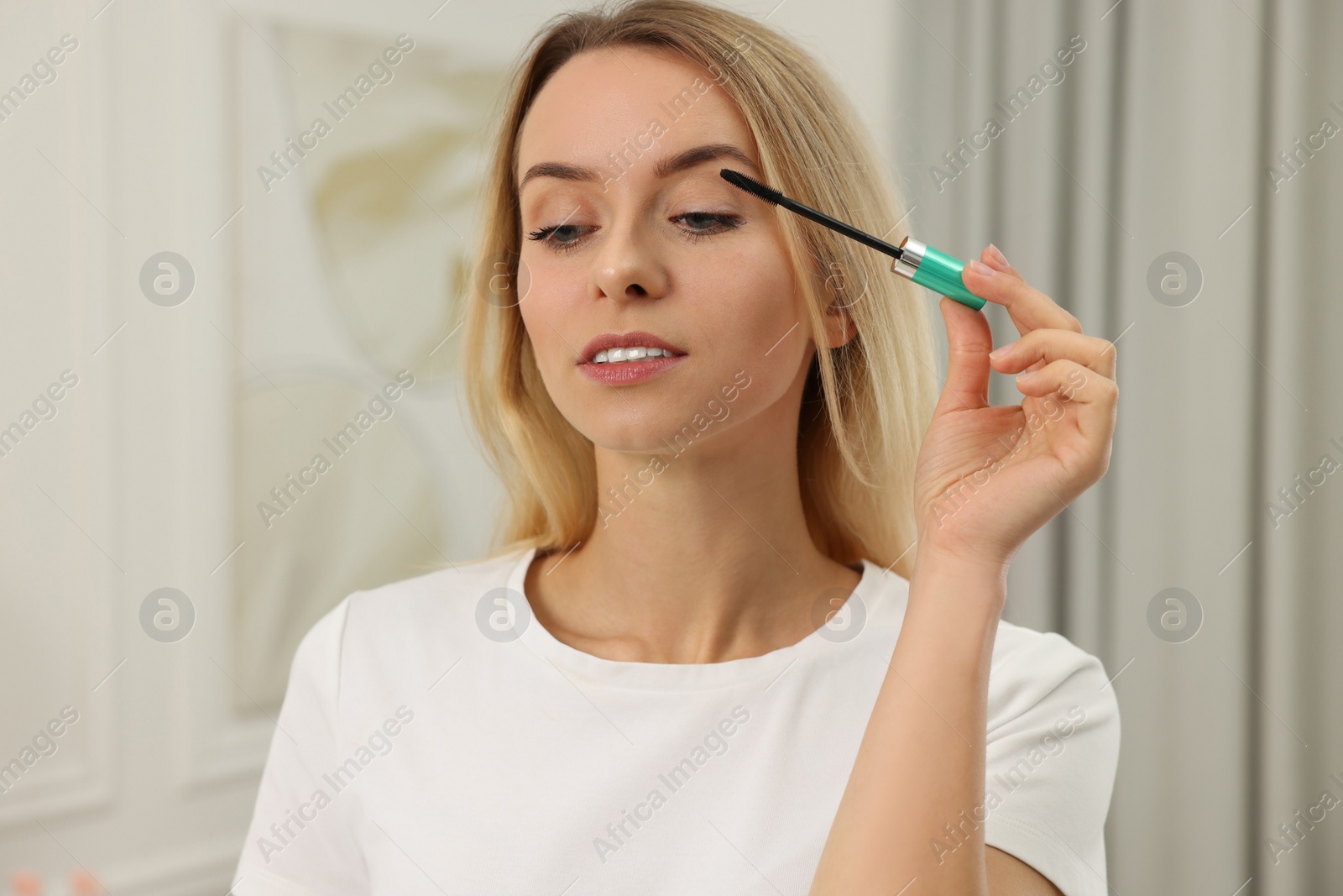 Photo of Beautiful woman applying mascara with brush indoors