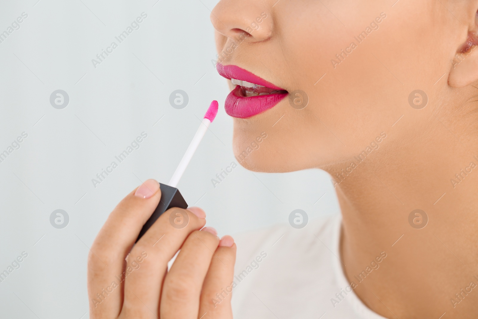 Photo of Beautiful woman applying liquid lipstick on light background, closeup