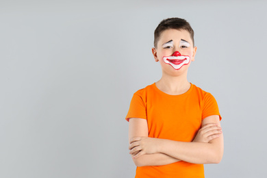 Photo of Preteen boy with clown makeup on light grey background, space for text. April fool's day