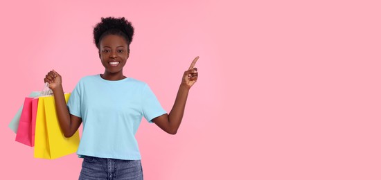 Photo of Happy young woman with shopping bags pointing at something on pink background. Space for text