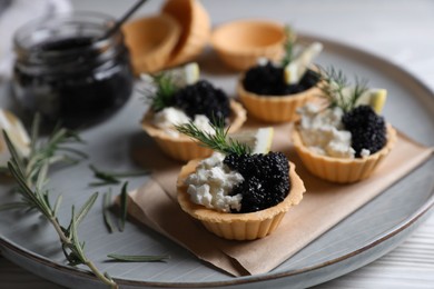 Photo of Delicious tartlets with black caviar, cream cheese and lemon served on white wooden table, closeup