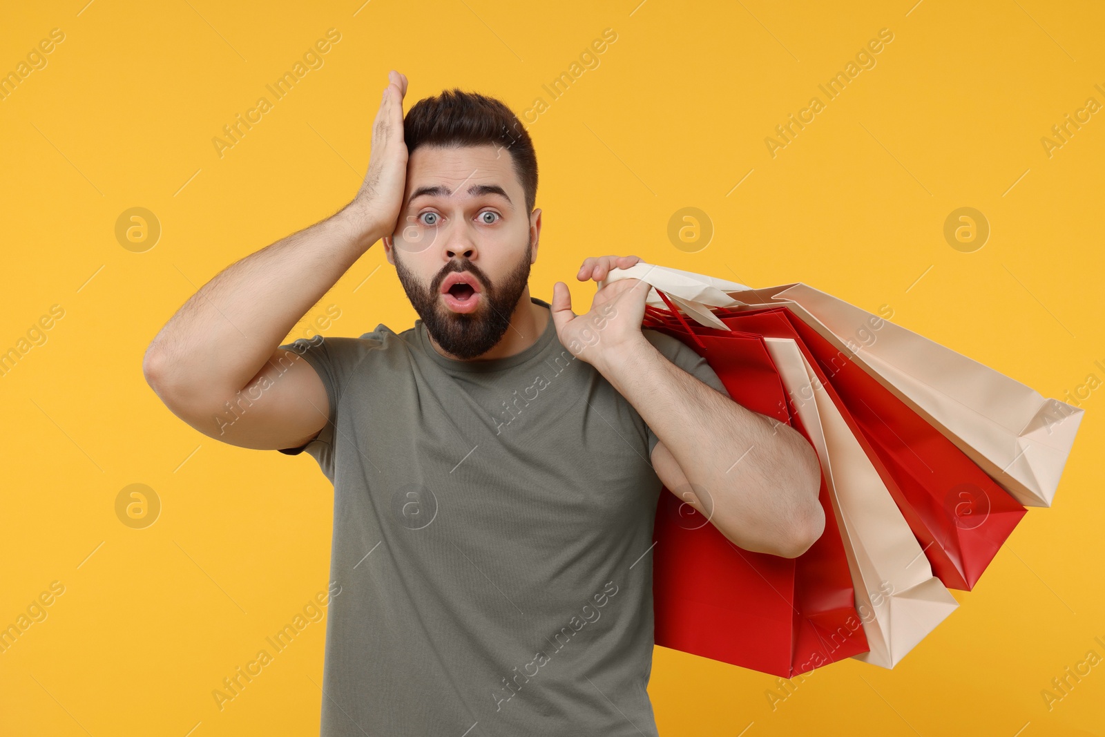 Photo of Shocked man with many paper shopping bags on orange background