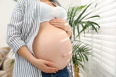 Photo of Pregnant woman near window at home, closeup
