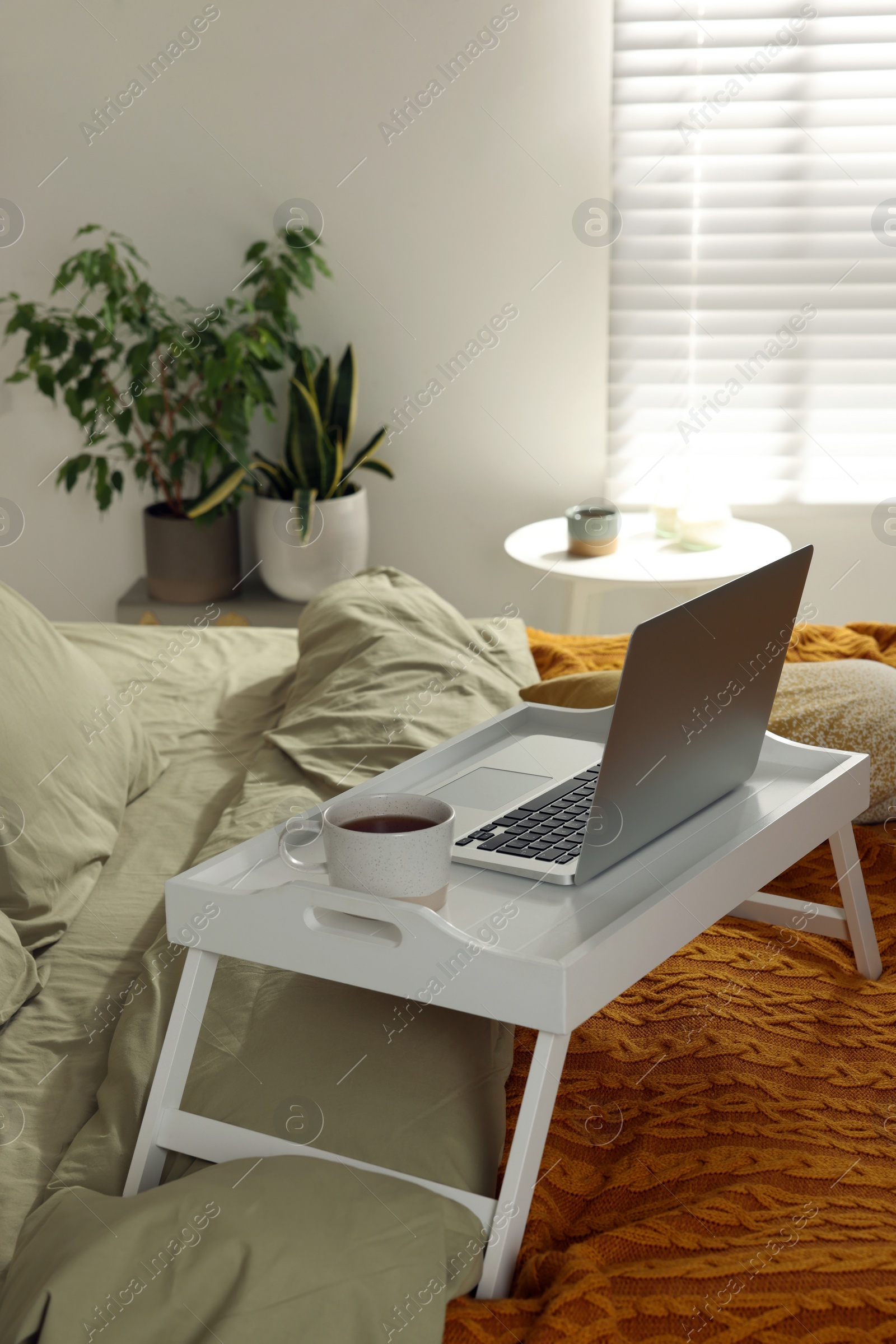 Photo of White tray with modern laptop and cup of aromatic tea on bed indoors