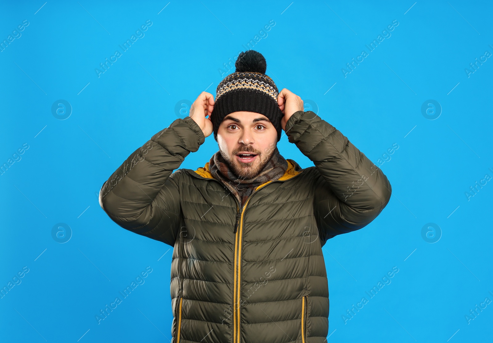 Photo of Young man in warm clothes on blue background. Winter vacation