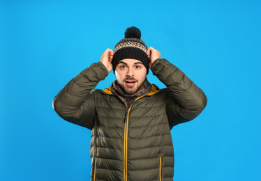 Young man in warm clothes on blue background. Winter vacation