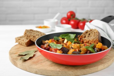 Photo of Dish with tasty ratatouille, bread and basil on white wooden table
