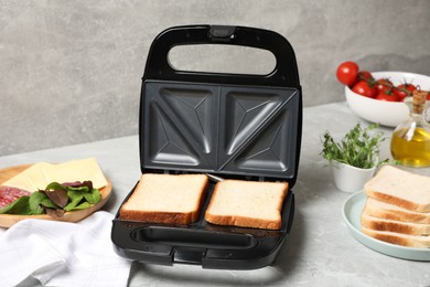 Modern sandwich maker with bread slices and different products on light grey table