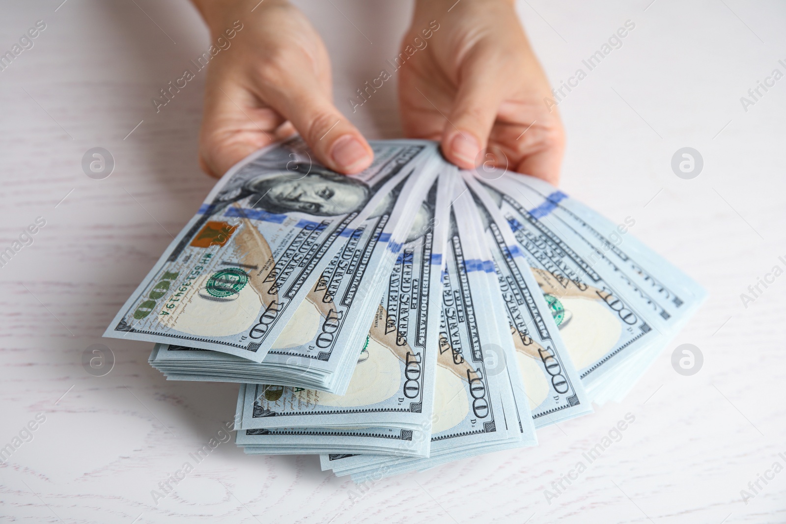 Photo of Woman holding dollar banknotes at white wooden table, closeup