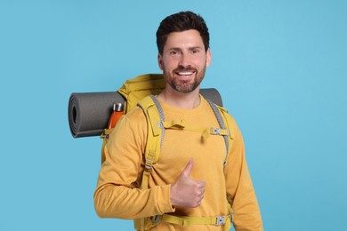 Photo of Happy man with backpack showing thumb up on light blue background. Active tourism