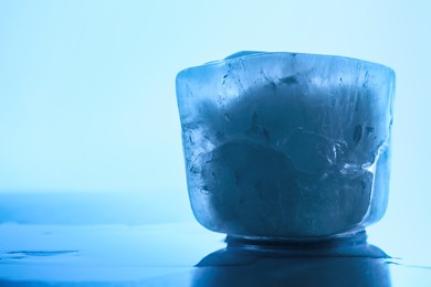 Photo of One crystal clear ice cube on light blue background, closeup and space for text. Color tone effect