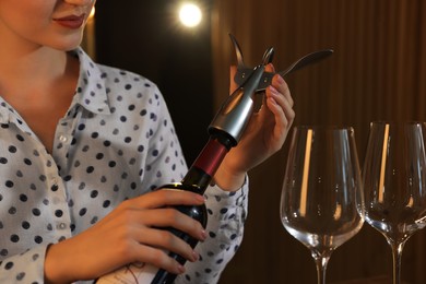 Romantic dinner. Woman opening wine bottle with corkscrew indoors, closeup