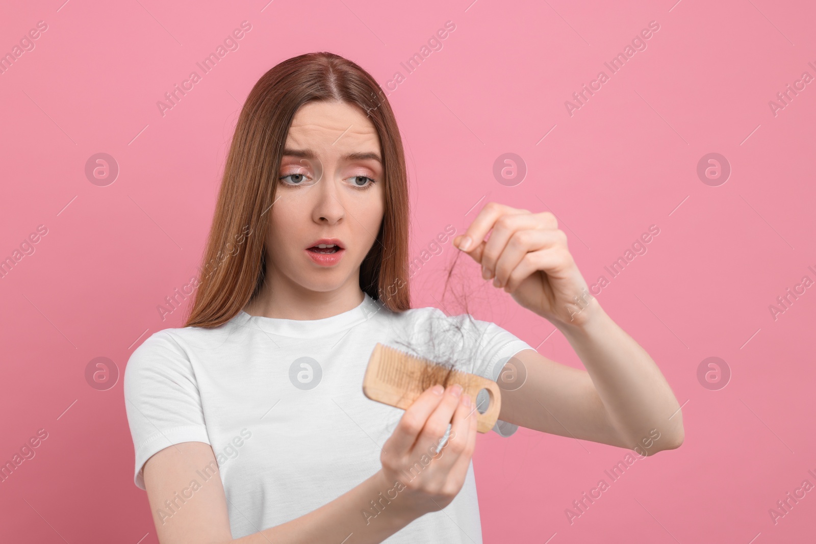 Photo of Emotional woman untangling her lost hair from comb on pink background. Alopecia problem