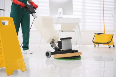 Photo of Professional janitor cleaning parquet floor with polishing machine in office, closeup