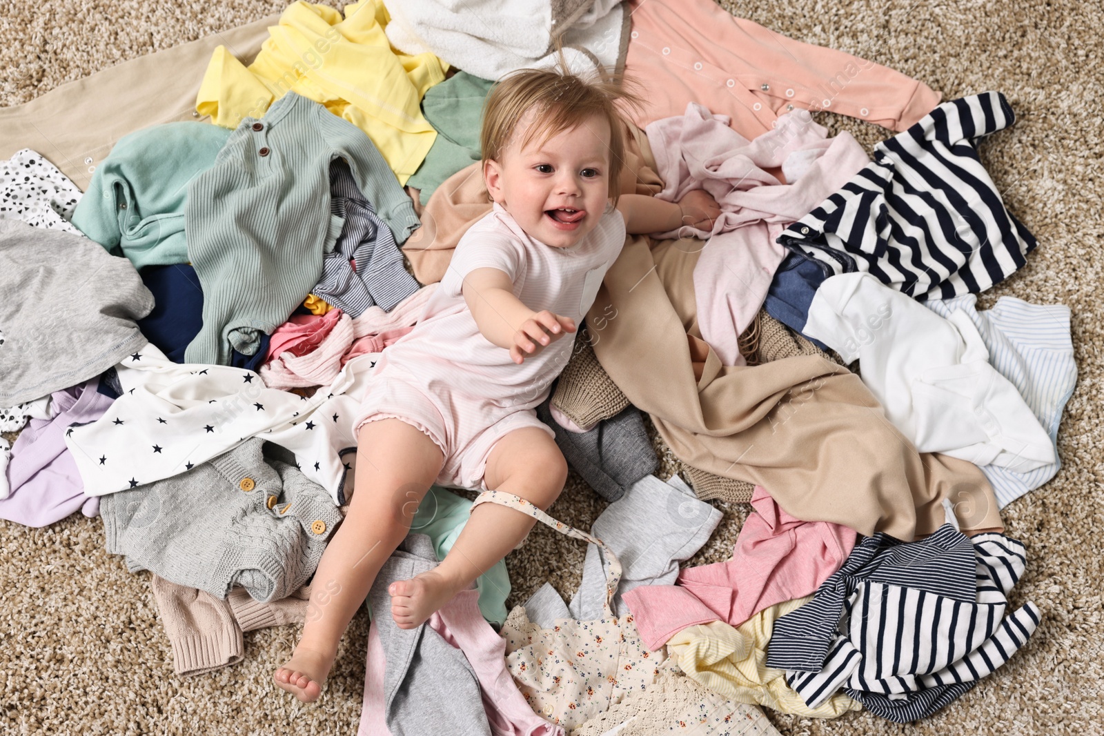 Photo of Little girl and pile of baby clothes on carpet