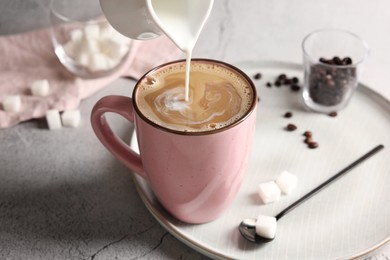 Photo of Pouring milk into cup with coffee on light grey textured table, closeup