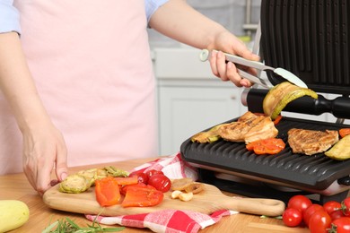 Photo of Woman cooking different products with electric grill at wooden table in kitchen, closeup