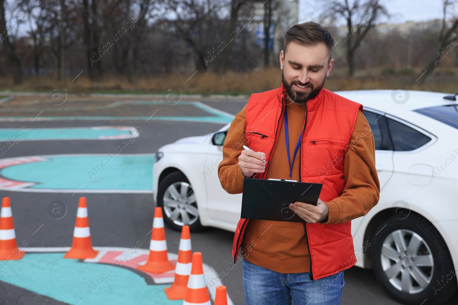 Photo of Instructor with clipboard near car on test track. Driving school