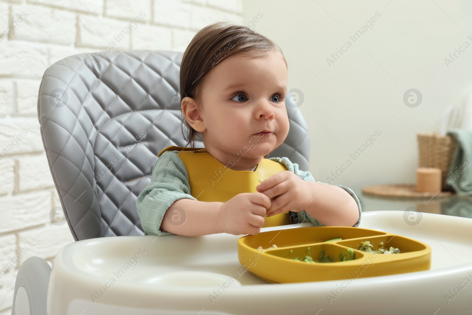 Photo of Cute little baby eating healthy food in high chair indoors