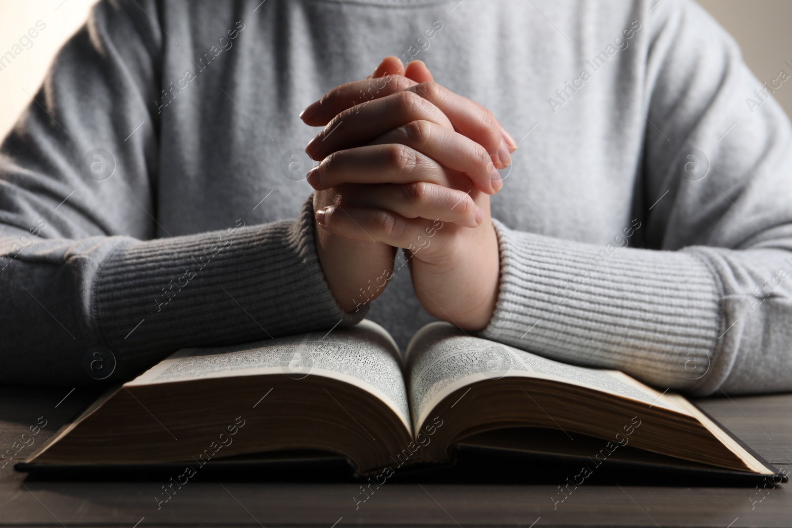 Photo of Woman holding hands clasped while praying over Bible at wooden table, closeup