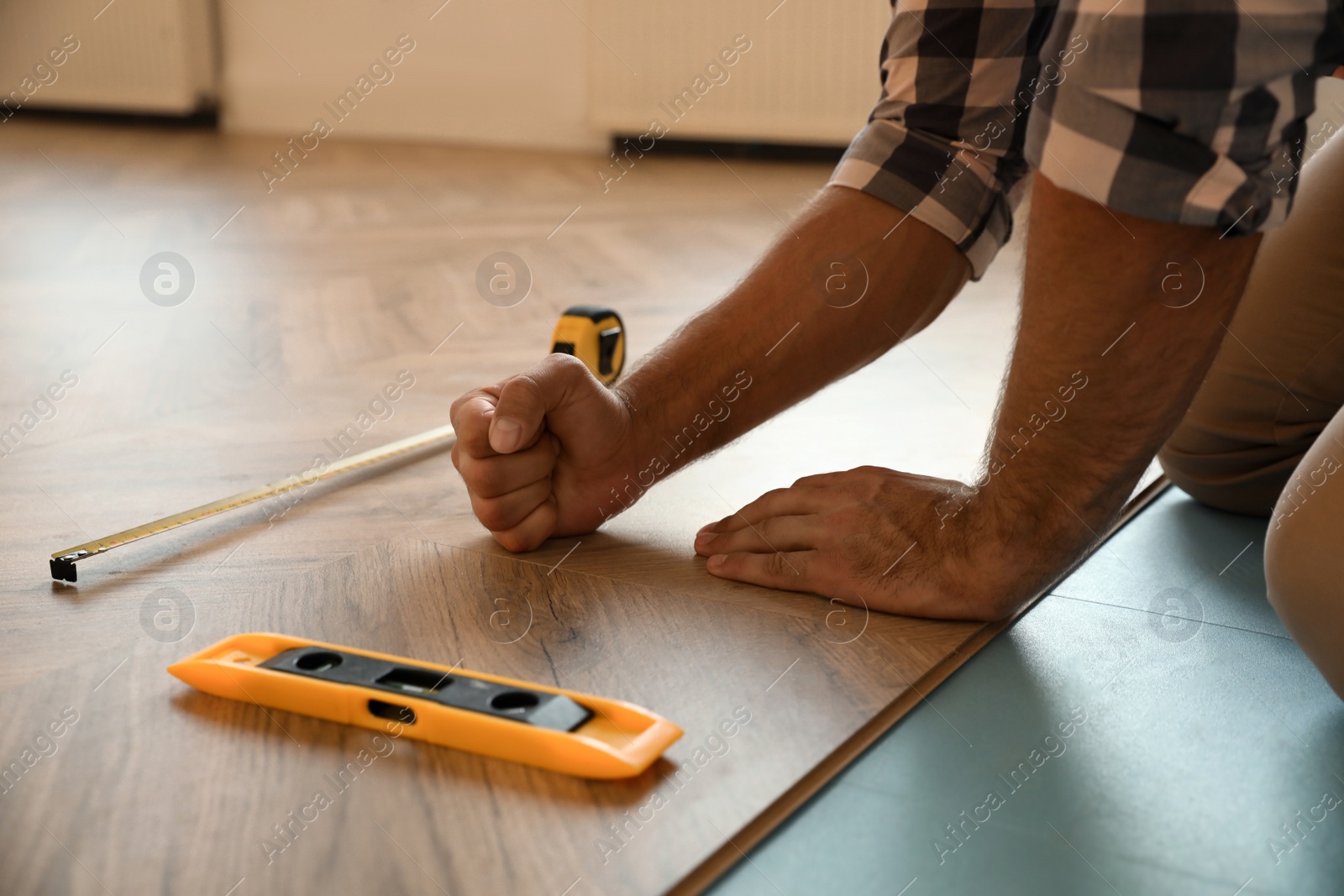 Photo of Professional worker installing new parquet flooring indoors, closeup