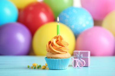 Photo of Delicious birthday cupcake with burning candle and gift on light blue wooden table