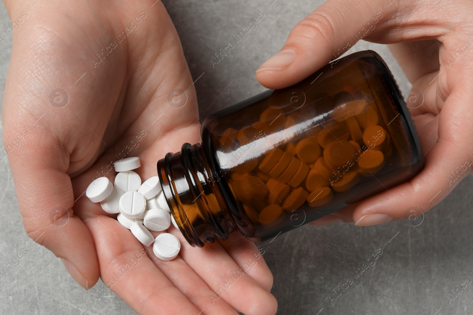 Photo of Woman pouring pills from bottle onto hand at light grey table, closeup