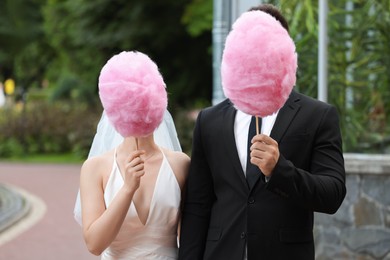 Photo of Bride and groom covering their faces with cotton candies outdoors
