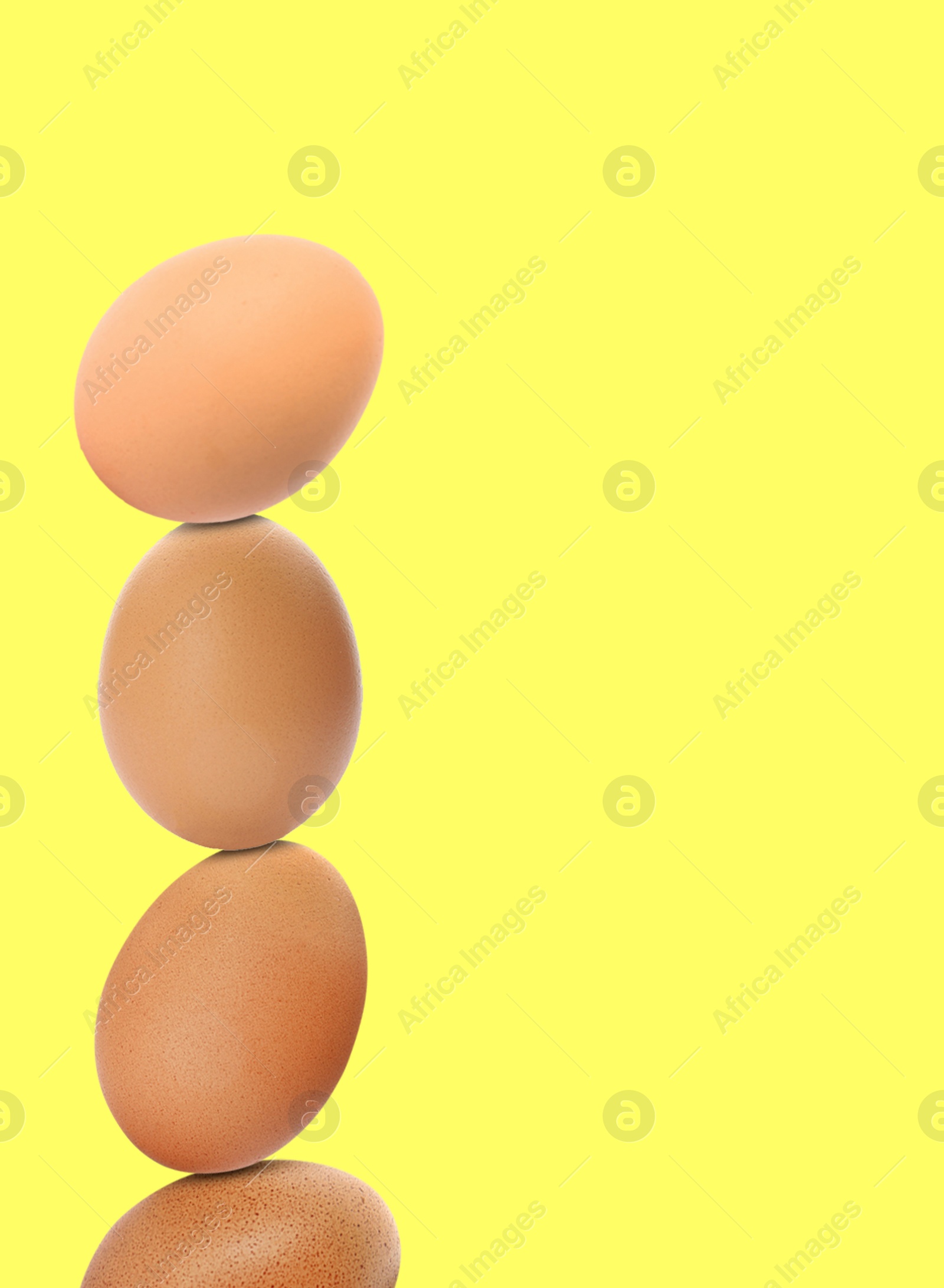 Image of Stacked fresh chicken eggs against light yellow background. Space for text