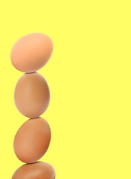 Stacked fresh chicken eggs against light yellow background. Space for text