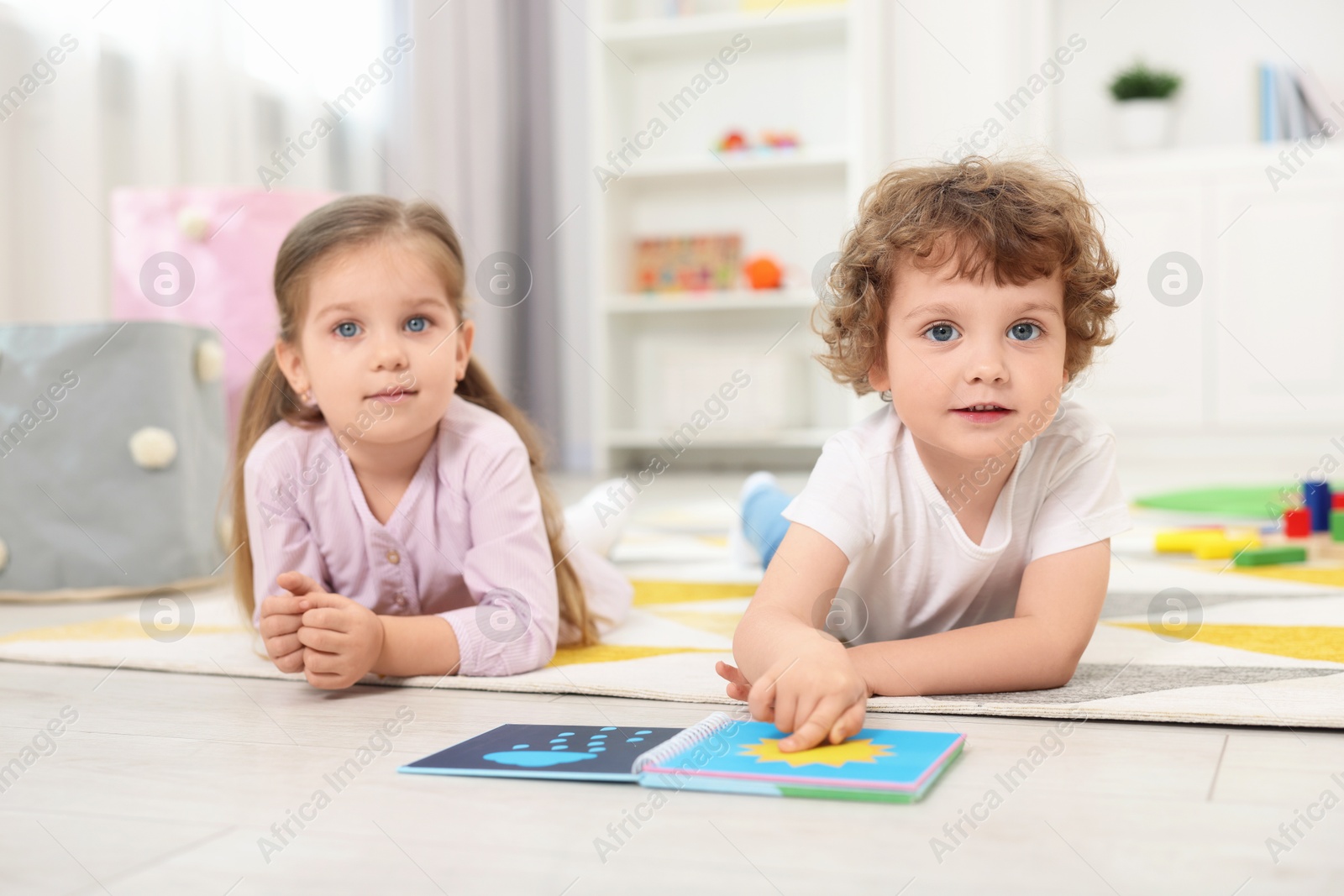 Photo of Cute little children reading book on floor in kindergarten