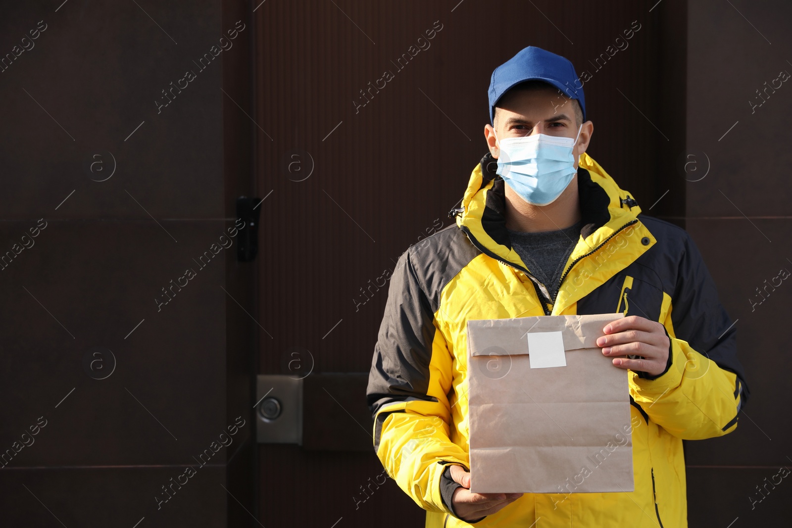 Photo of Courier in medical mask holding takeaway food outdoors. Delivery service during quarantine due to Covid-19 outbreak