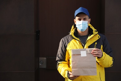 Courier in medical mask holding takeaway food outdoors. Delivery service during quarantine due to Covid-19 outbreak