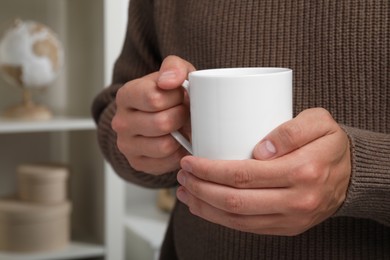 Photo of Man holding white mug indoors, closeup. Space for text