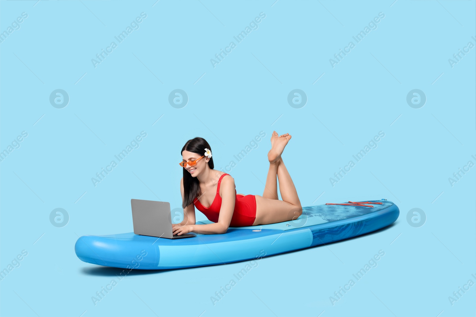 Photo of Happy woman with laptop on SUP board against light blue background