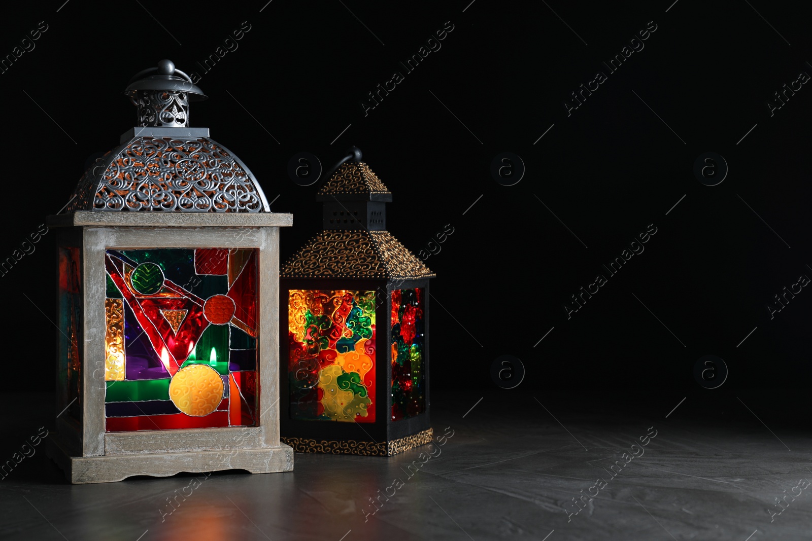 Photo of Decorative Arabic lanterns on grey table against black background, space for text