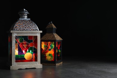 Photo of Decorative Arabic lanterns on grey table against black background, space for text
