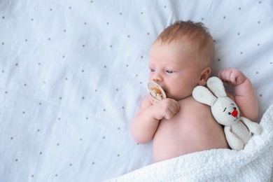 Cute newborn baby with toy lying in bed, top view. Space for text